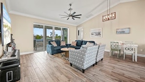 A spacious living room with a ceiling fan, a blue sofa set, a patterned armchair, and a dining area with a white table and chairs. - Ibis Landing - Boat Lift & Gulf Access (Fort Myers Beach)
