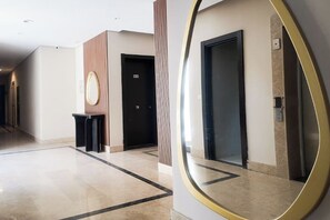 En hotelgang med gulv af poleret marmor, et rundt spejl og to sorte døre.