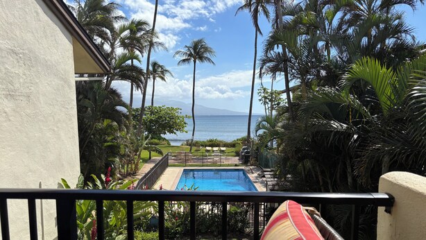 A pool area with a view of the ocean, surrounded by palm trees and a fenced deck. - New Remodel Beachfront Maalaea Condo w/ AC (Wailuku)