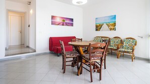 Ein Essbereich mit einem runden Holztisch, sechs Korbstühlen, einem roten Sofa und zwei an der Wand hängenden Bildern.