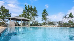 A clear swimming pool with a wooden deck and lounge chairs, surrounded by tall trees and a covered pavilion. - Rookery III 4009 | 3BR Cottage | 1/2 Mile to Beach | Screened-In Porch (Fort Morgan)