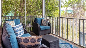 A covered outdoor seating area with wicker furniture and patterned cushions, overlooking a lush green landscape. - Rookery III 4009 | 3BR Cottage | 1/2 Mile to Beach | Screened-In Porch (Fort Morgan)