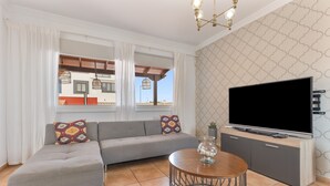 A living room with a grey sofa, a round coffee table, a TV on a cabinet, and a patterned wall. - Vacation Villa 'Atlantic Ocean Private Pool' with Sea View and Wi-Fi (Corralejo)