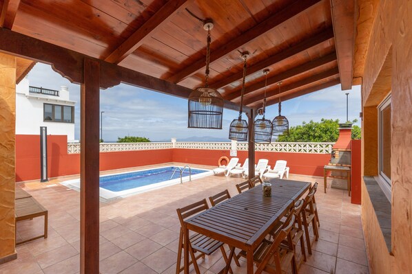 Un patio exterior con piscina, muebles de madera y jaulas de pájaros colgantes.