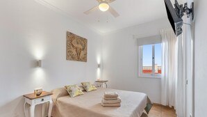 A bedroom with a bed, bedside tables, a ceiling fan, a window with curtains, and a wall-mounted artwork. - Vacation Villa 'Atlantic Ocean Private Pool' with Sea View and Wi-Fi (Corralejo)