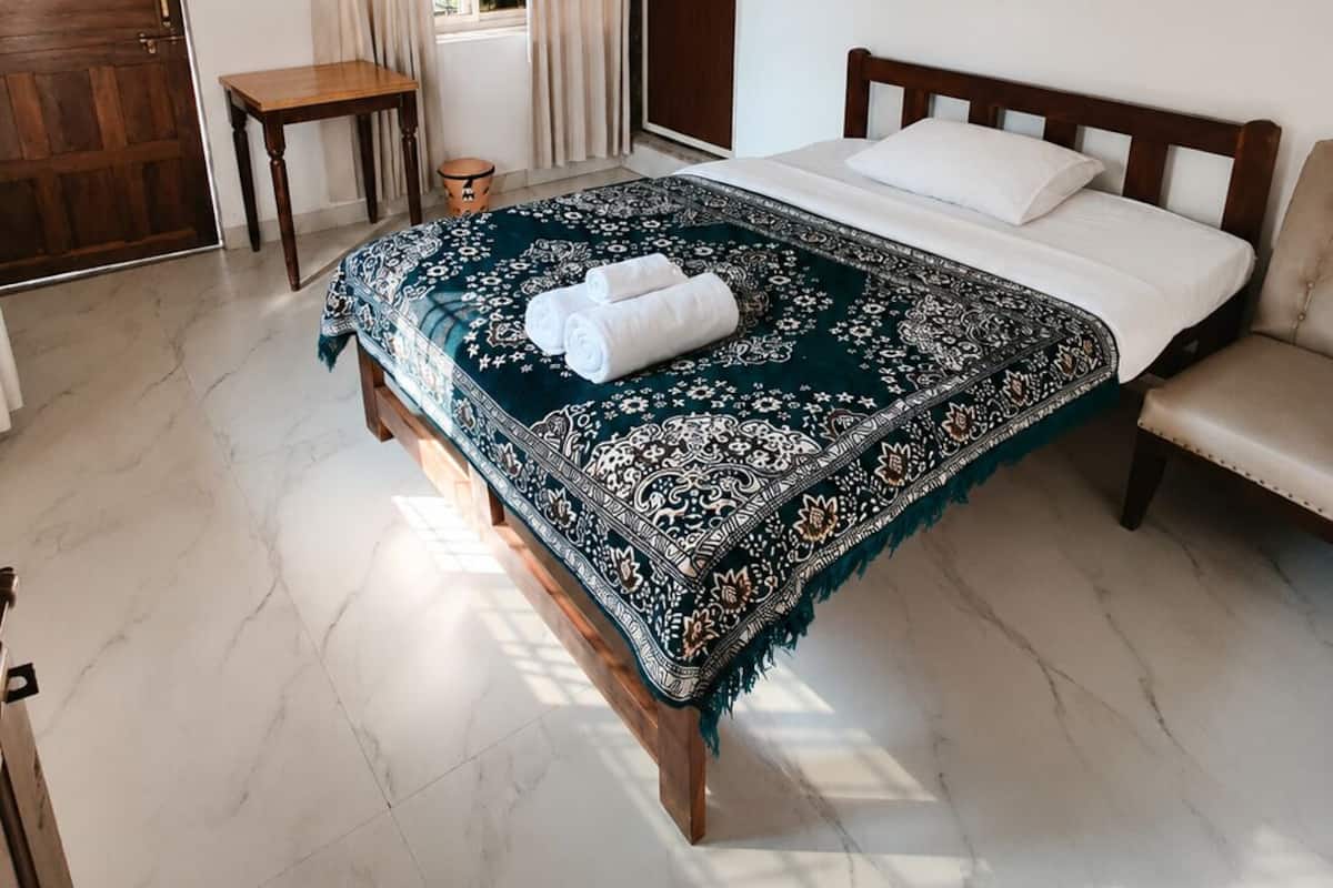 Een slaapkamer met een bed, een plafondventilator, een houten deur, een raam met gordijnen, een klein tafeltje en een ingelijst schilderij aan de muur.