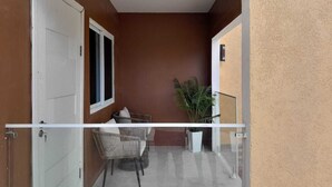 Ein Balkon mit weißer Reling, einem Blumentopf und einem Korbstuhl.