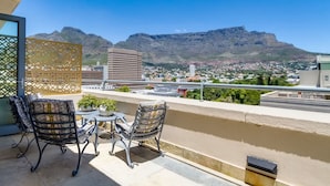 Un balcon avec deux chaises et une petite table, d’où l’on peut admirer une vue sur la ville, avec des montagnes en arrière-plan.
