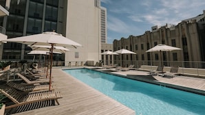 Un espace piscine doté de chaises longues et de parasols, entouré d’immeubles modernes.