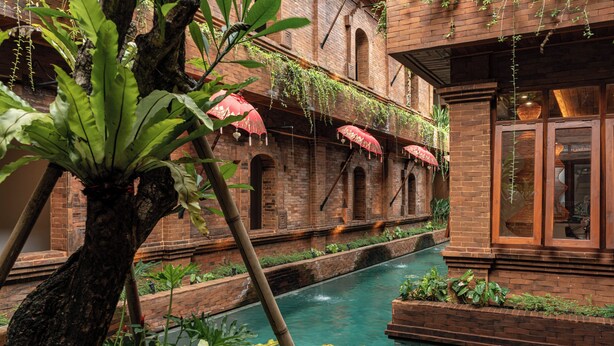 A courtyard with a brick building, a small water channel, and hanging red umbrellas.