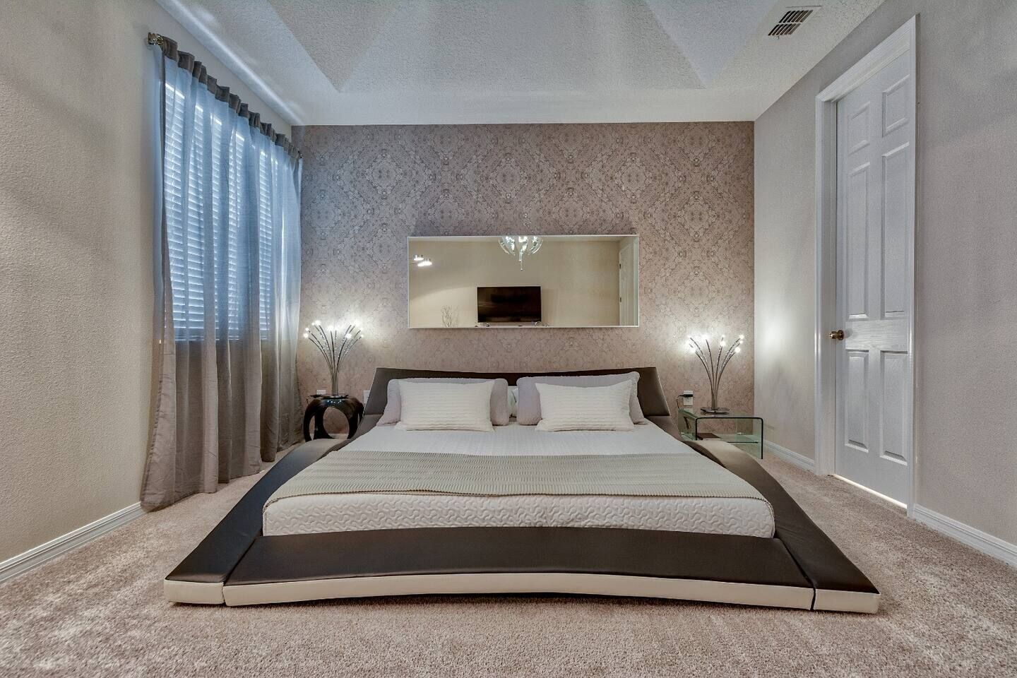 A bedroom with a large bed, a mirror above the bed, and a door on the right.