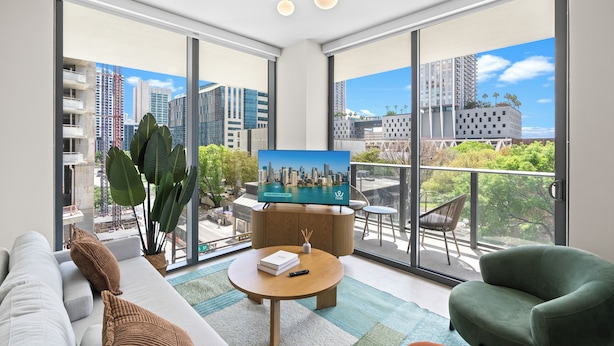 A modern living room with a large TV, a sofa, a green armchair, and a balcony with a city view. - 11 Ne Worldcenter Experience - We Host (Miami)