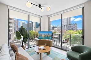 Una sala de estar moderna con un televisor grande, un sofá, un sillón verde y un balcón con vistas a la ciudad.