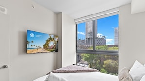 A hotel room with a bed, a TV mounted on the wall, and a large window offering a view of buildings and trees. - 11 Ne Worldcenter Experience - We Host (Miami)