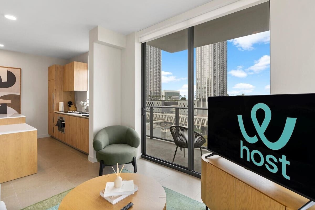 Une chambre d’hôtel moderne dotée d’un balcon, d’une kitchenette, d’une télévision et offrant une vue sur de hauts immeubles.