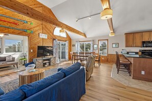 A spacious living area with a large sofa, wooden ceiling beams, and a dining area with a kitchen in the background. - Shorely Dreaming: Private Pool | Hot Tub | Dog Only (Corolla)