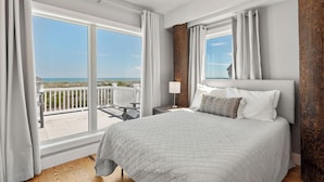 Ein Schlafzimmer mit einem großen Bett, einem Nachttisch, einer Lampe und Blick auf den Strand.