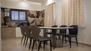 Un comedor con una mesa y sillas, una ventana con persianas, un dispensador de agua y un microondas en la encimera.