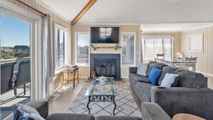A spacious living room with a fireplace, comfortable seating, and large windows. - Sunshine and Whiskey: Pets Allowed | Private Pool | Private Hot Tub (Corolla)