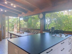 A kitchen with a large island, a clock, and a view of greenery outside. - Posidonie by Interhome (L'Ile Rousse)