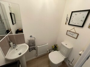 A modern bathroom with a white sink, toilet, and radiator. There are decorative items like a framed quote and a small sign on the wall. - Bright and Airey House (Wellingborough)