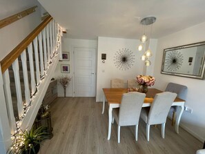 A dining area with a wooden table, grey chairs, a vase of flowers, and a chandelier. - Bright and Airey House (Wellingborough)