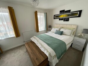 A bedroom with a bed, bedside tables, a bench, a radiator, and a window with curtains. - Bright and Airey House (Wellingborough)
