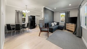 A modern living room with a dining area, grey curtains, a flat-screen TV, and a wooden cabinet. - Stylish Private Studio • Minutes to Downtown & UCD Med Center (Sacramento)