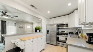 A modern kitchen with white cabinets, stainless steel appliances, and a wooden countertop.