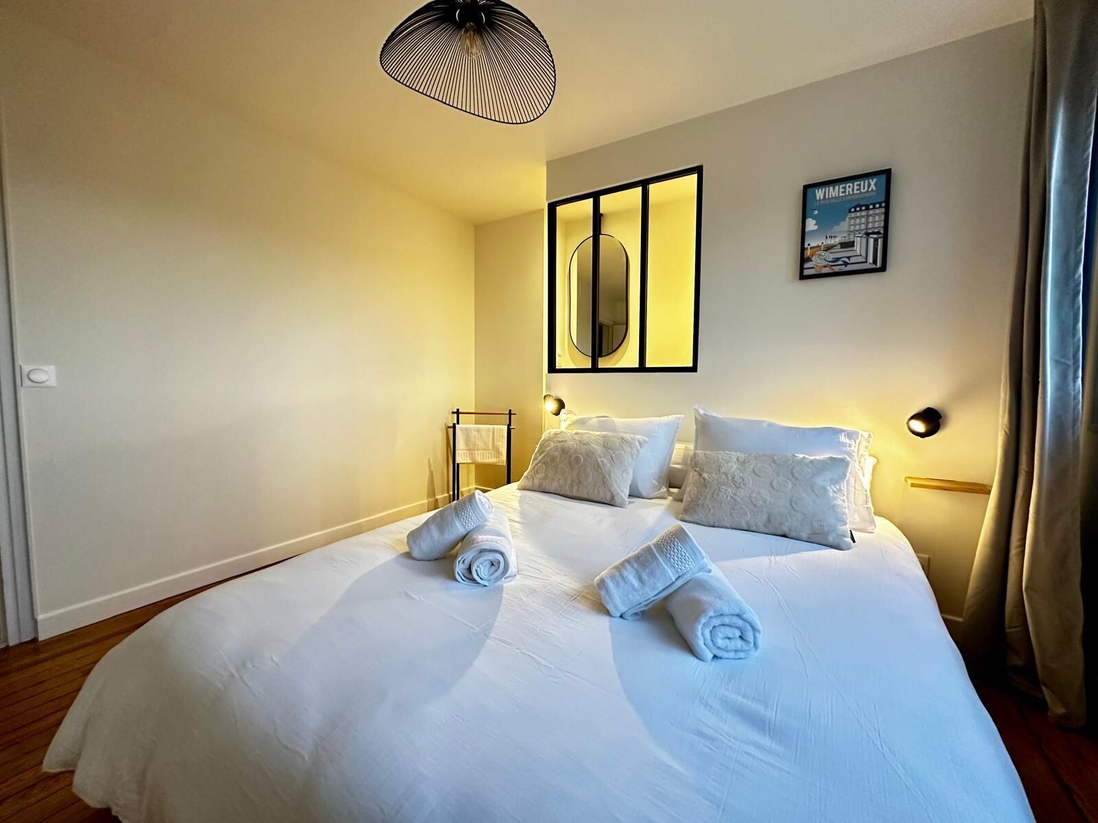 A hotel room with a large bed, a wall-mounted mirror, and a poster on the wall.
