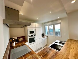 A modern kitchen with white cabinets, a stainless steel range hood, a built-in microwave, an oven, and a window with a view of the sea. - La Maison Des Degrés 6 persons and 1 baby (Boulogne-sur-Mer)