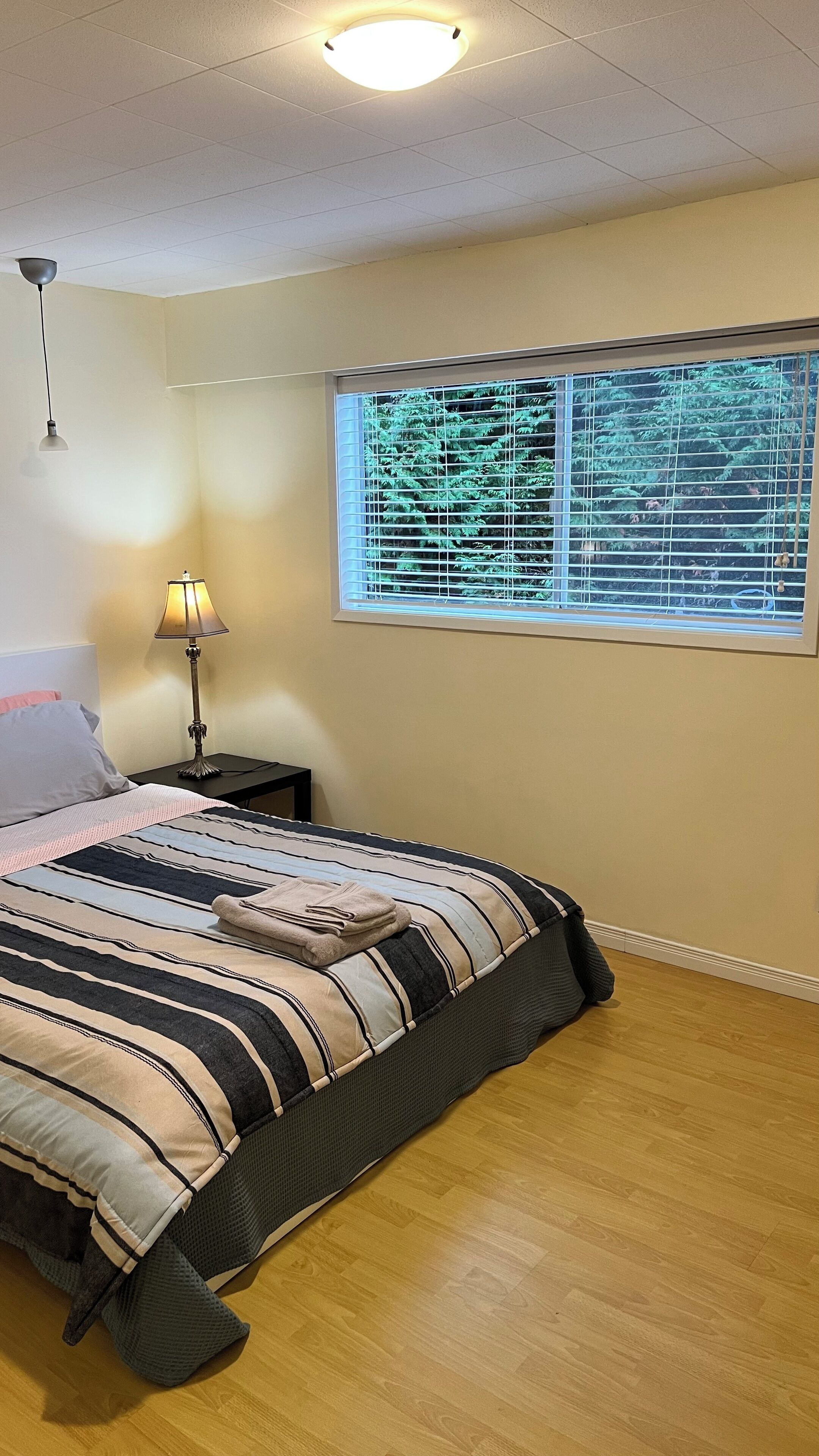 Een slaapkamer met een bed, nachtkastje, lamp en een raam met zonwering.