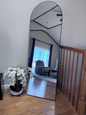 Un grand miroir reflétant une pièce avec un plancher en bois, une chaise et une table.