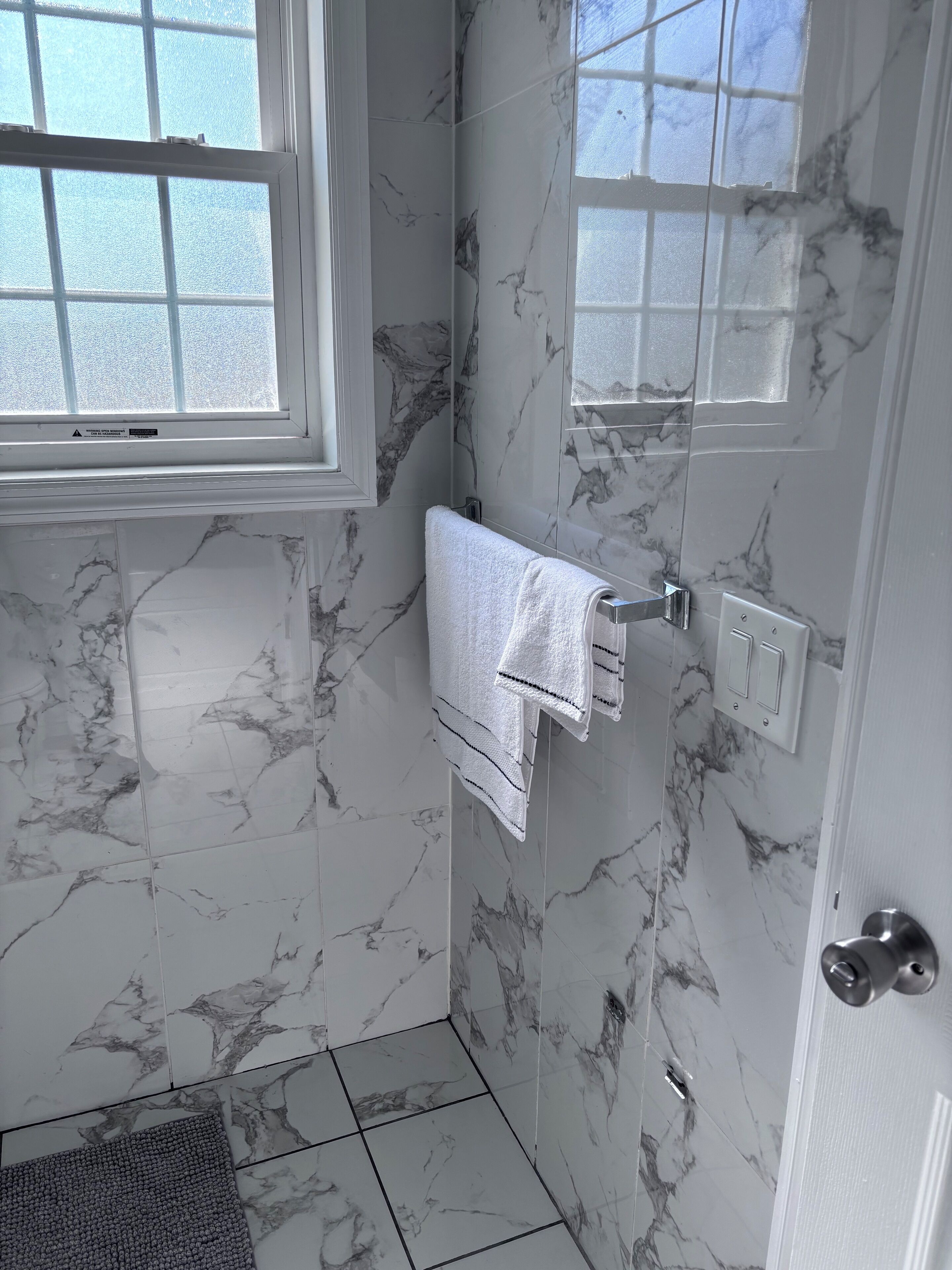 A bathroom with marble walls, a white towel hanging on a rack, and a window with blinds.