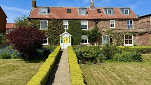 A traditional brick house with a red-tiled roof, a central entrance with a white door, and a small white structure in the front garden. - Bay View House is one of Yorkshire's premier coastal retreats. Featuring hot tub, fire pit and 4 stu (Bridlington)