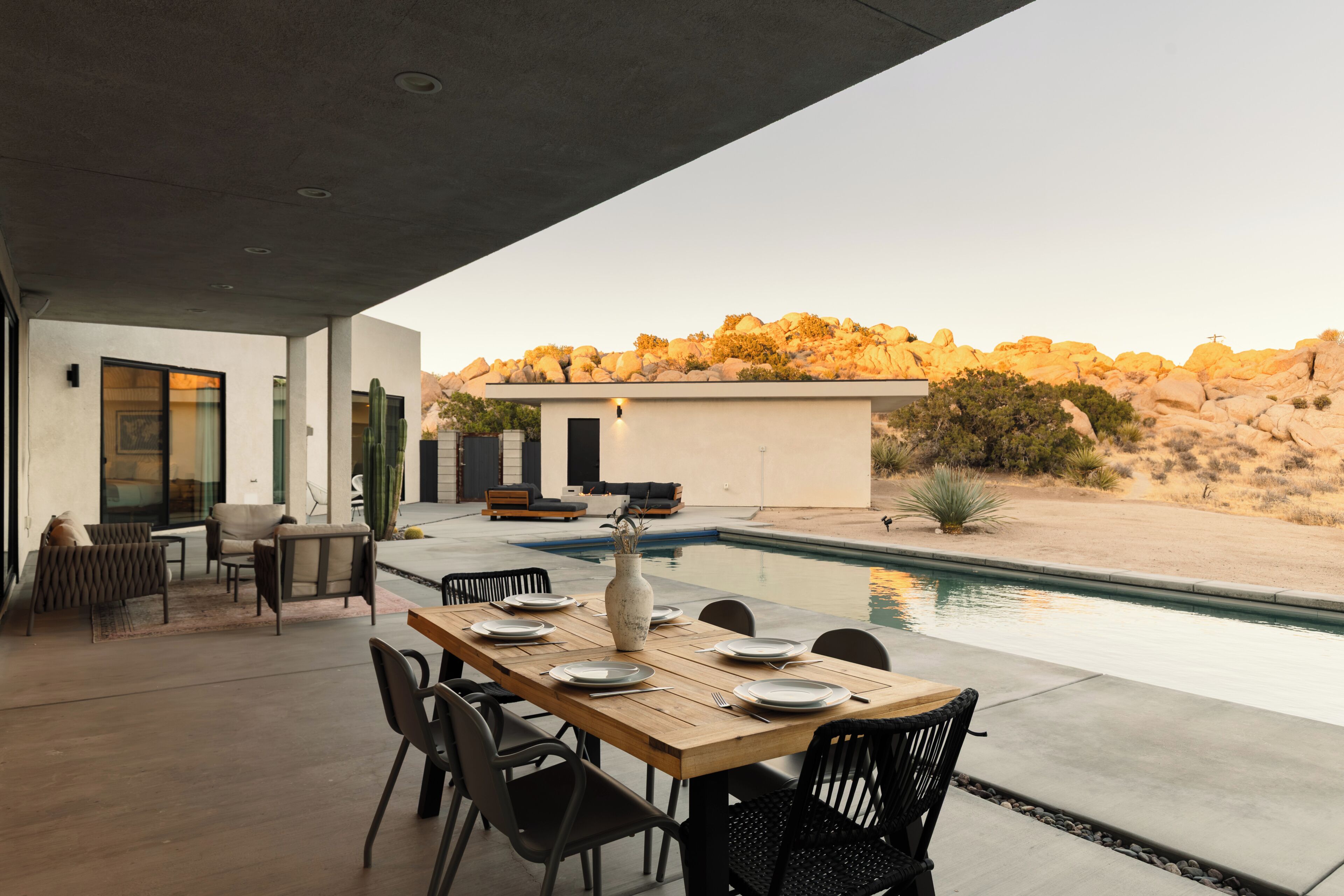 Un espace extérieur aménagé pour les repas, avec une piscine, un cactus et une vue sur un paysage désertique.