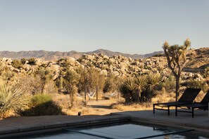 A desert landscape with a pool, lounge chairs, and a hammock. - Mars Landing - Pool / Spa / Boulders / View / BBQ / Stargazing (Yucca Valley)