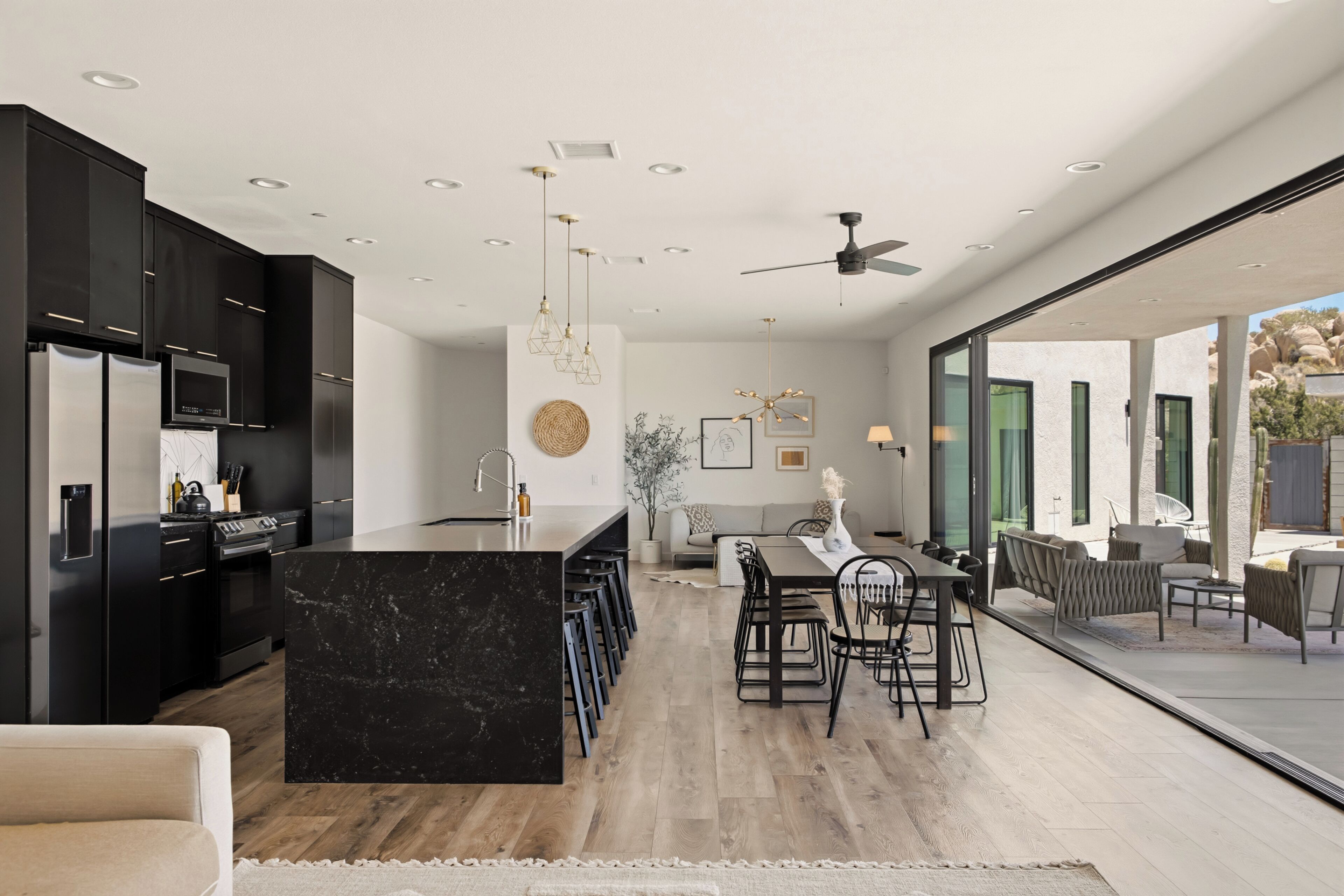 Une cuisine moderne avec des meubles de couleur sombre, un îlot en marbre et un coin repas comprenant une grande table et des chaises.