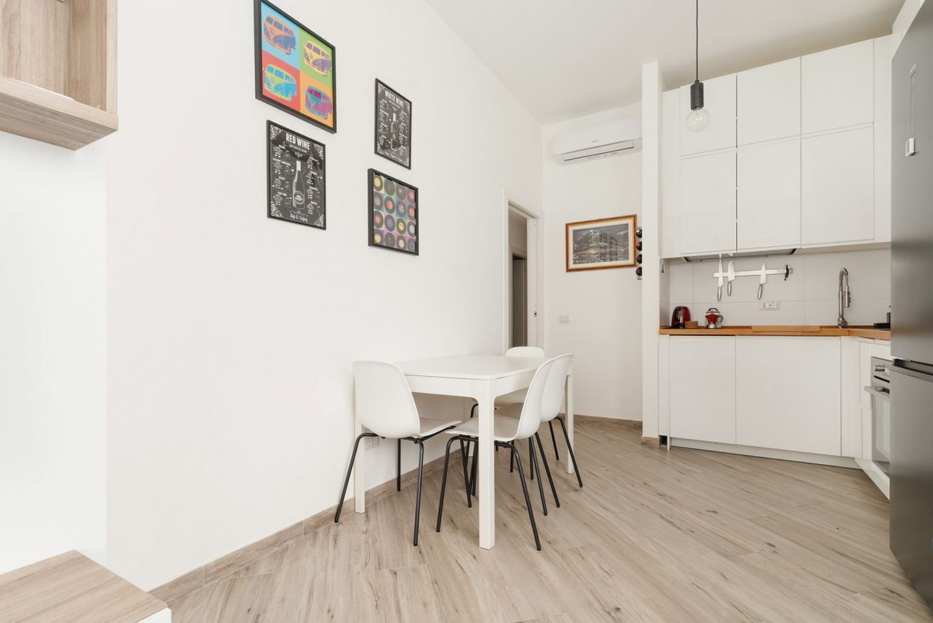 Een moderne keuken met witte kasten, een houten aanrechtblad en een eethoek met een witte tafel en stoelen.