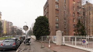 Una strada con auto parcheggiate, un recinto bianco e un edificio con diverse finestre.