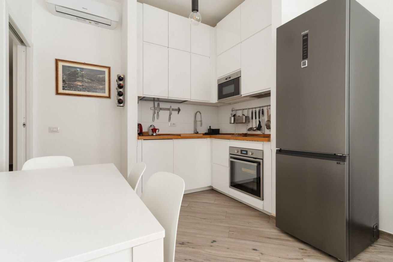 Een keuken met witte kasten, een roestvrijstalen koelkast, een magnetron en een oven.