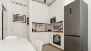 Una cucina con mobili bianchi, un frigorifero in acciaio inox, un forno a microonde e un forno.