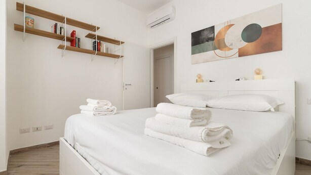 Una camera da letto con un letto, asciugamani bianchi, una libreria, un quadro e una porta.