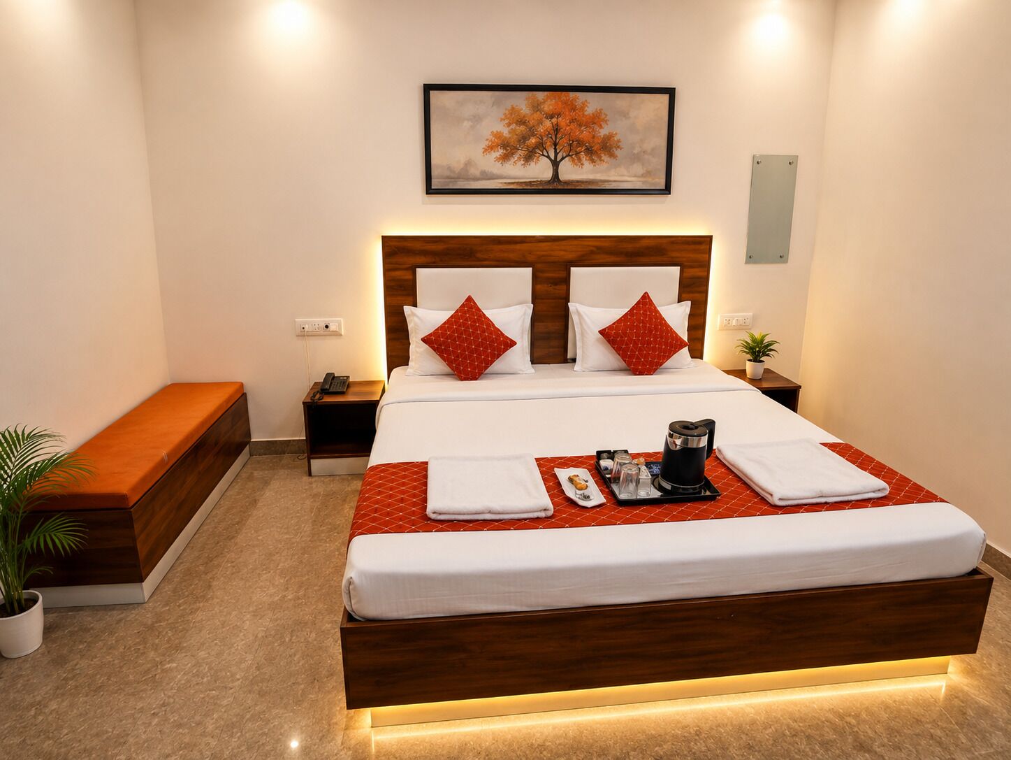 Habitación de hotel con una cama grande, una mesita de noche con teléfono, un banco, una planta y un cuadro en la pared.