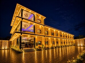 Un edificio de varios pisos con ventanas iluminadas y un área de entrada pavimentada.