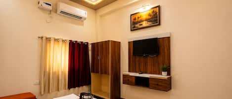A hotel room with a bed, a TV mounted on the wall, a painting above the TV, and a window with curtains.