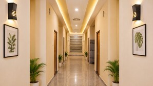 A hotel hallway with a marble floor, framed botanical prints on the walls, potted plants, and a staircase at the end. - Shree Venkatesh Niliyam 300 M Ram Temple (Ayodhya)