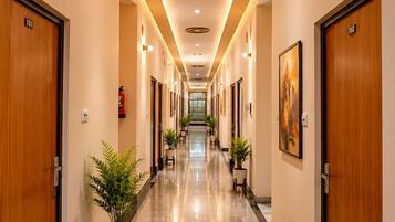 Un pasillo de hotel con puertas de madera numeradas 101 y 102, plantas en macetas y un cuadro en la pared.