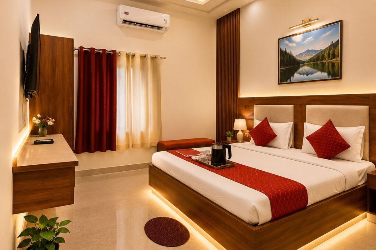A hotel room with a large bed, bedside tables, a TV, an air conditioning unit, and a painting on the wall.