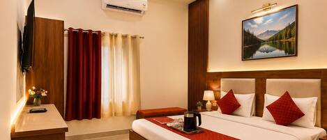 A hotel room with a large bed, bedside tables, a TV, an air conditioning unit, and a painting on the wall.